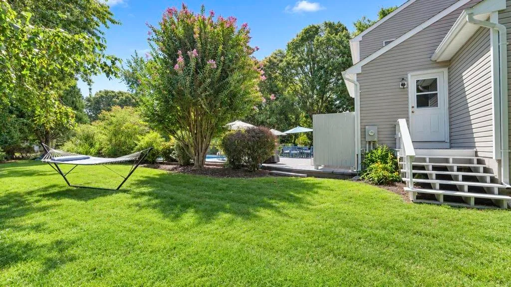 A grassy backyard beside a gray house, with a hammock and flowering tree.