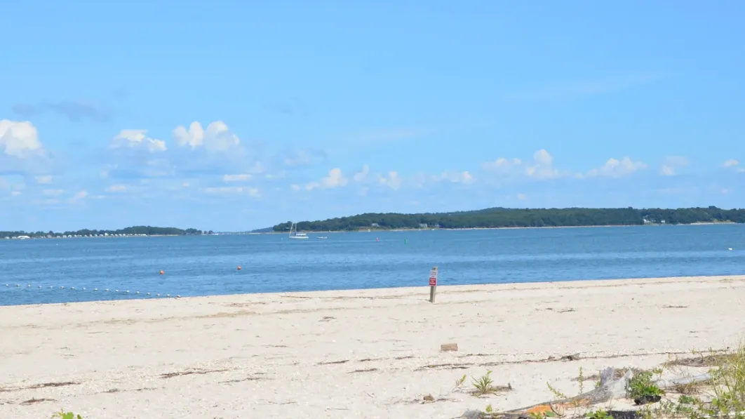 A sandy beach borders calm blue water beneath a partly cloudy sky.