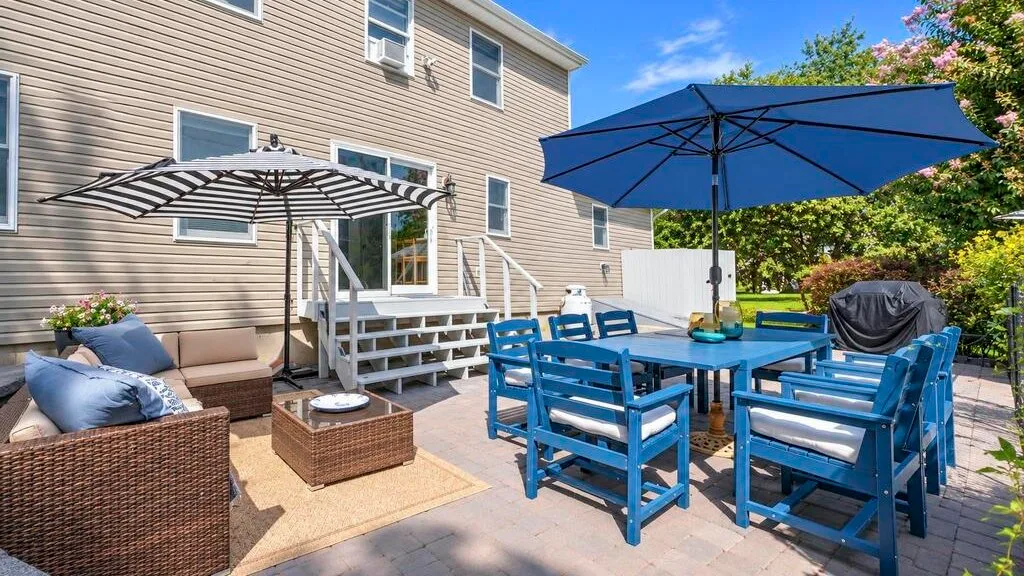 An outdoor patio with blue dining chairs, umbrellas, and cushioned seating beside a house.