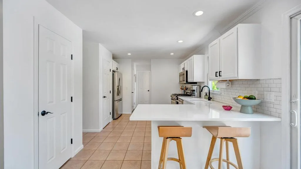 A bright kitchen with white cabinets, a large island, and two stools.