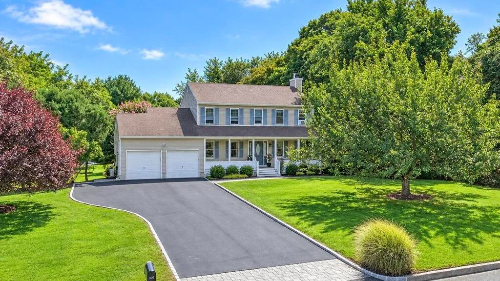 A two-story house stands beside a paved driveway and green lawn.