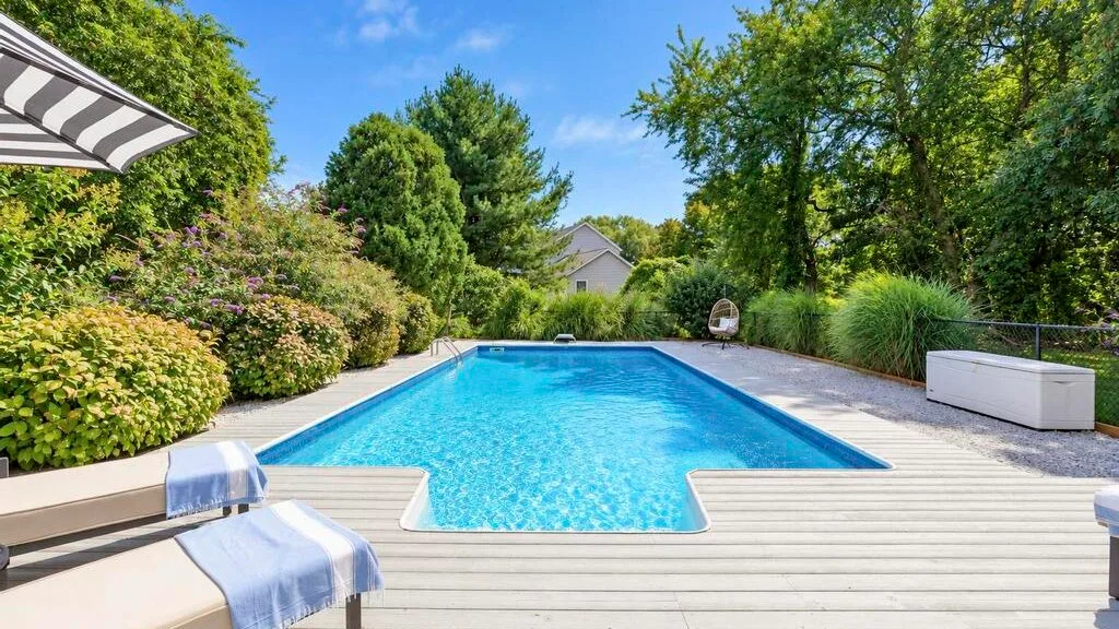 An outdoor swimming pool is surrounded by greenery and a deck.