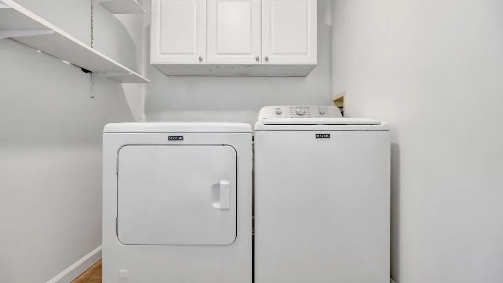 A laundry area with a washer and dryer beneath white cabinets.