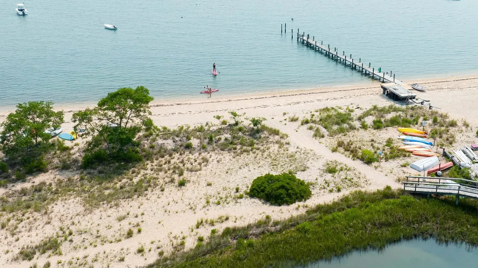 A sandy beach borders calm water, with a pier extending into the bay.