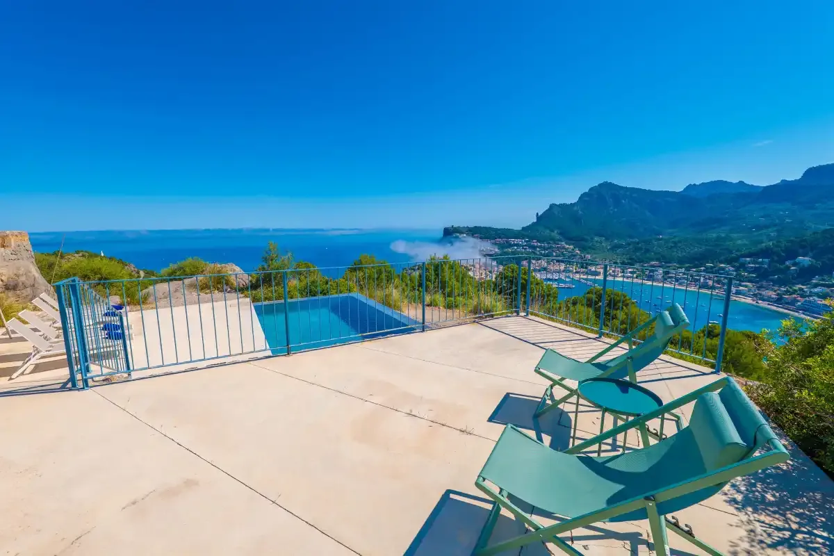 Una terraza soleada da a una bahía costera, con una piscina y asientos.