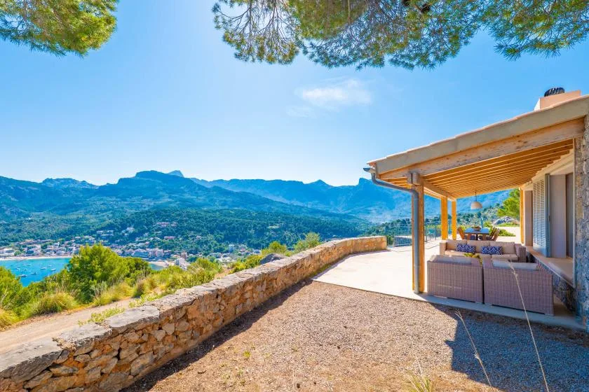 Una zona de estar cubierta da a una terraza de piedra y montañas lejanas.