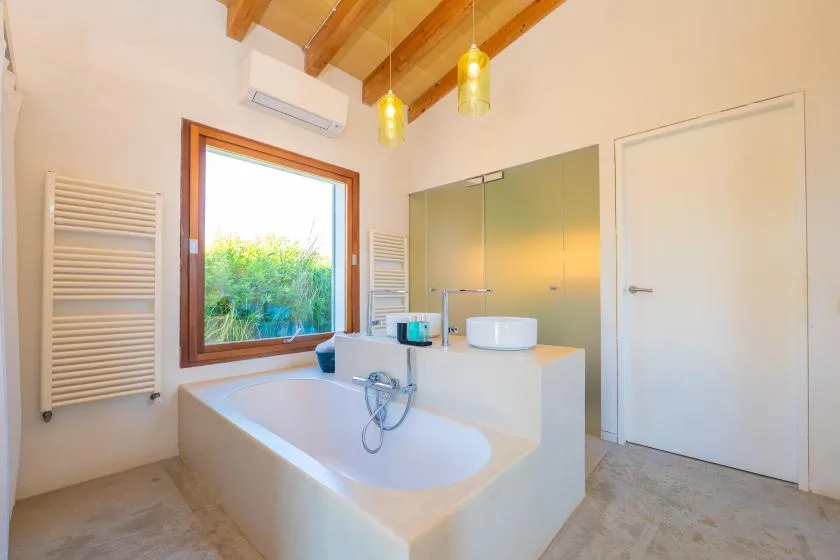 Un baño luminoso con bañera empotrada, lavabo y una ventana grande.