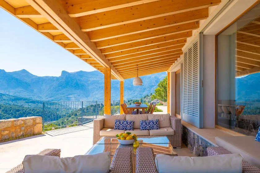 Una terraza exterior cubierta tiene asientos y vistas a las montañas.