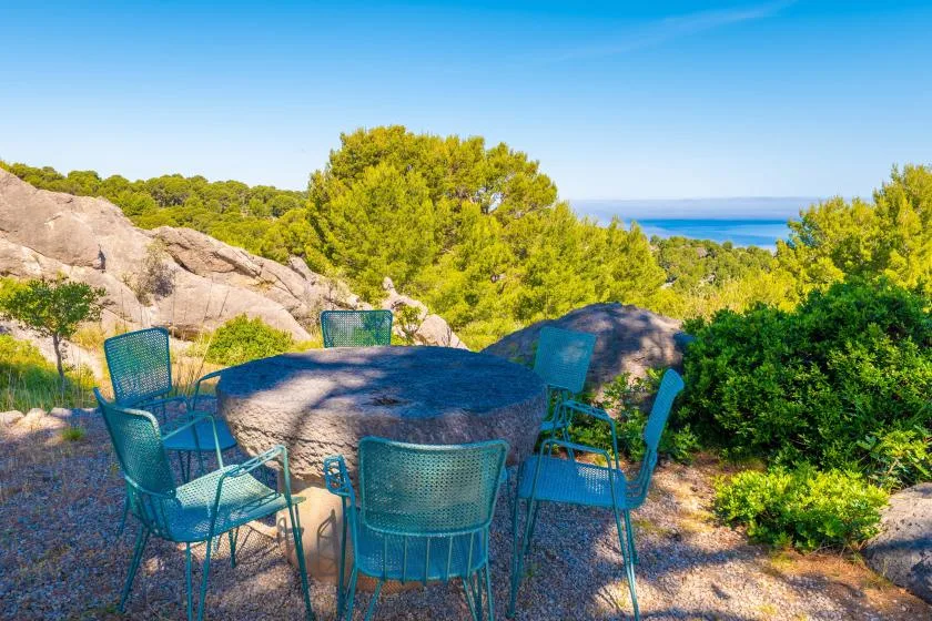 Una zona de estar al aire libre con una mesa entre árboles, con vistas al mar.