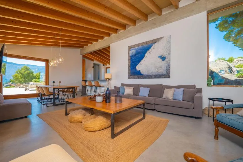 Una sala de estar con zona de asientos, mesa de centro y grandes ventanas.