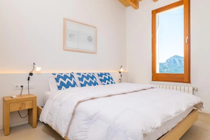 Un dormitorio luminoso con una cama vestida de blanco y una ventana amplia.