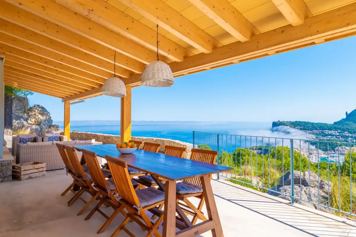 Una zona de comedor exterior cubierta mira al mar, con una mesa y sillas de madera.