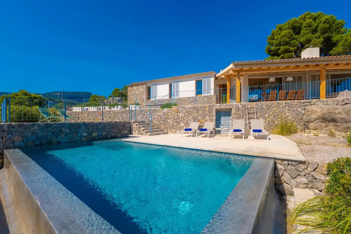 Una piscina al aire libre junto a una terraza de piedra y una casa.