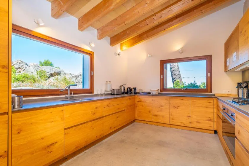 Una cocina luminosa con gabinetes de madera, un fregadero y ventanas grandes.