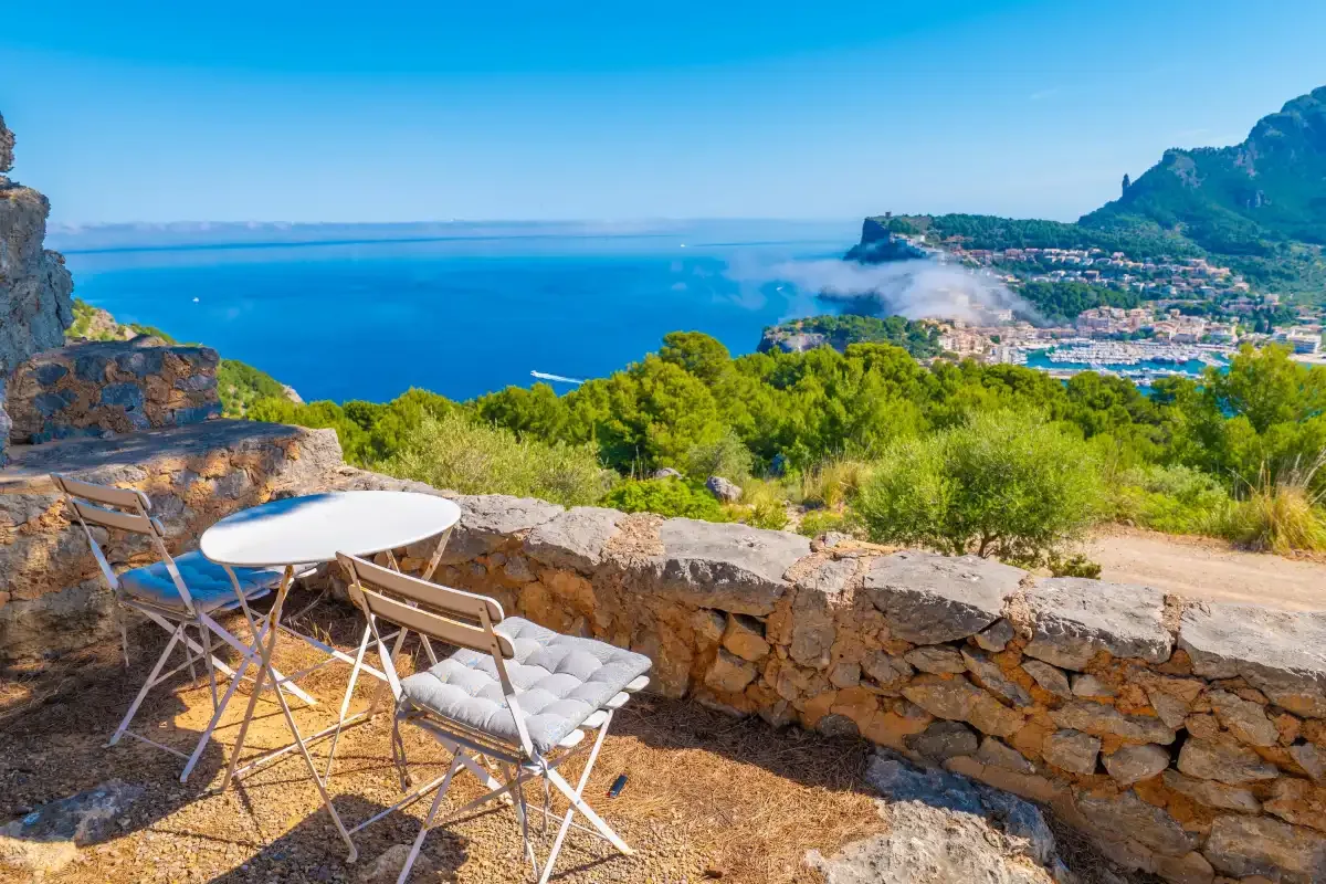 Una terraza de piedra mira al mar azul, con asientos al aire libre junto a un muro bajo de piedra.