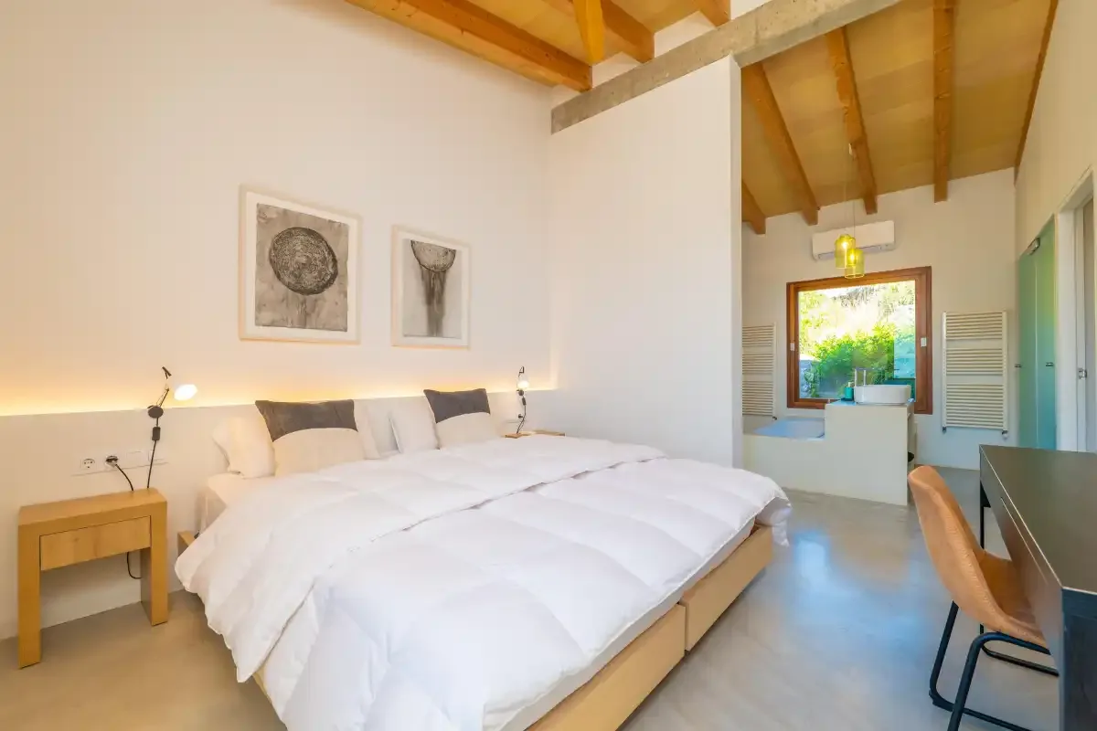 Un dormitorio luminoso con ropa de cama blanca, mesillas y vigas de madera vistas en el techo.