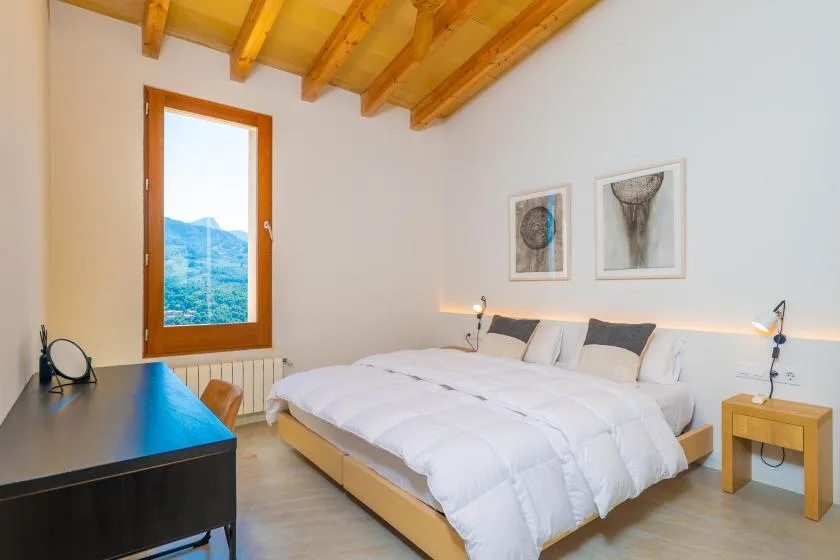 Un dormitorio con una cama grande, vigas de madera en el techo y una ventana con vistas a la vegetación.