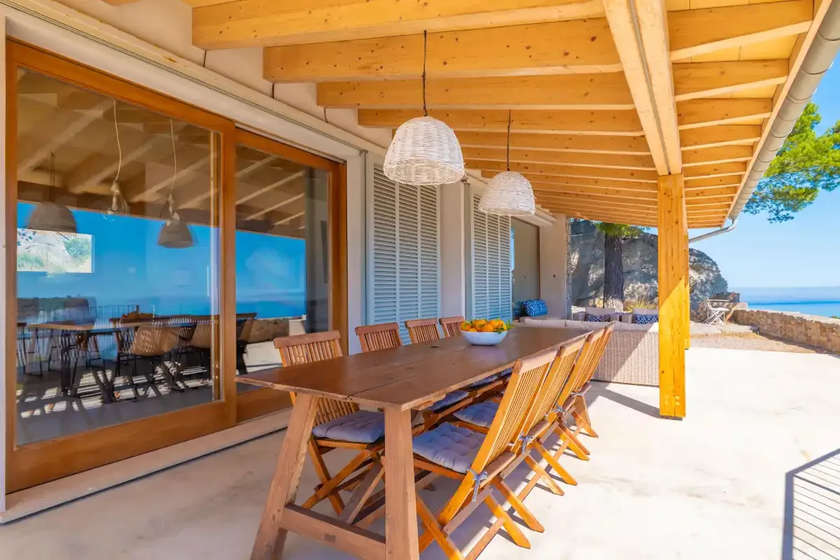 Una zona de comedor exterior cubierta con una mesa larga y asientos junto a puertas de vidrio.