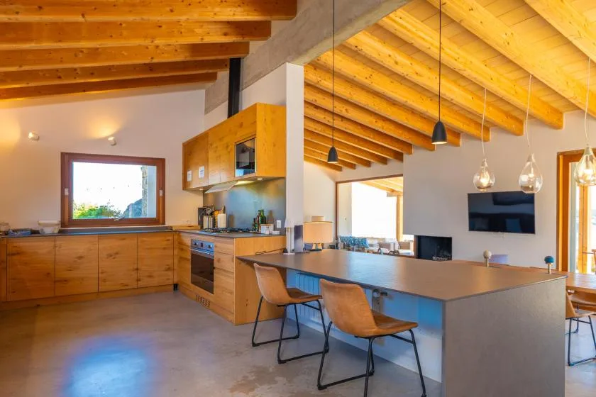 Una cocina abierta con zona de comedor tiene armarios de madera y una mesa larga.