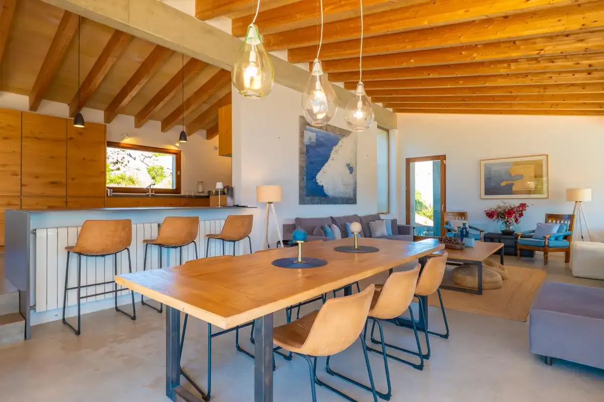 Un luminoso espacio abierto de comedor y sala de estar tiene una larga mesa de madera y asientos.