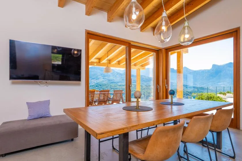 Un comedor con una mesa de madera y grandes ventanales con vistas a las montañas.