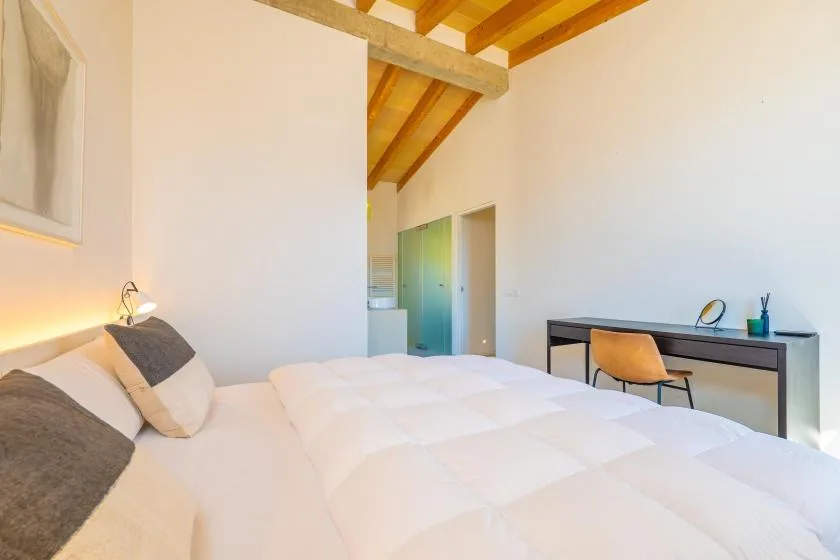 Un dormitorio luminoso con una cama y un escritorio bajo un techo inclinado de madera.
