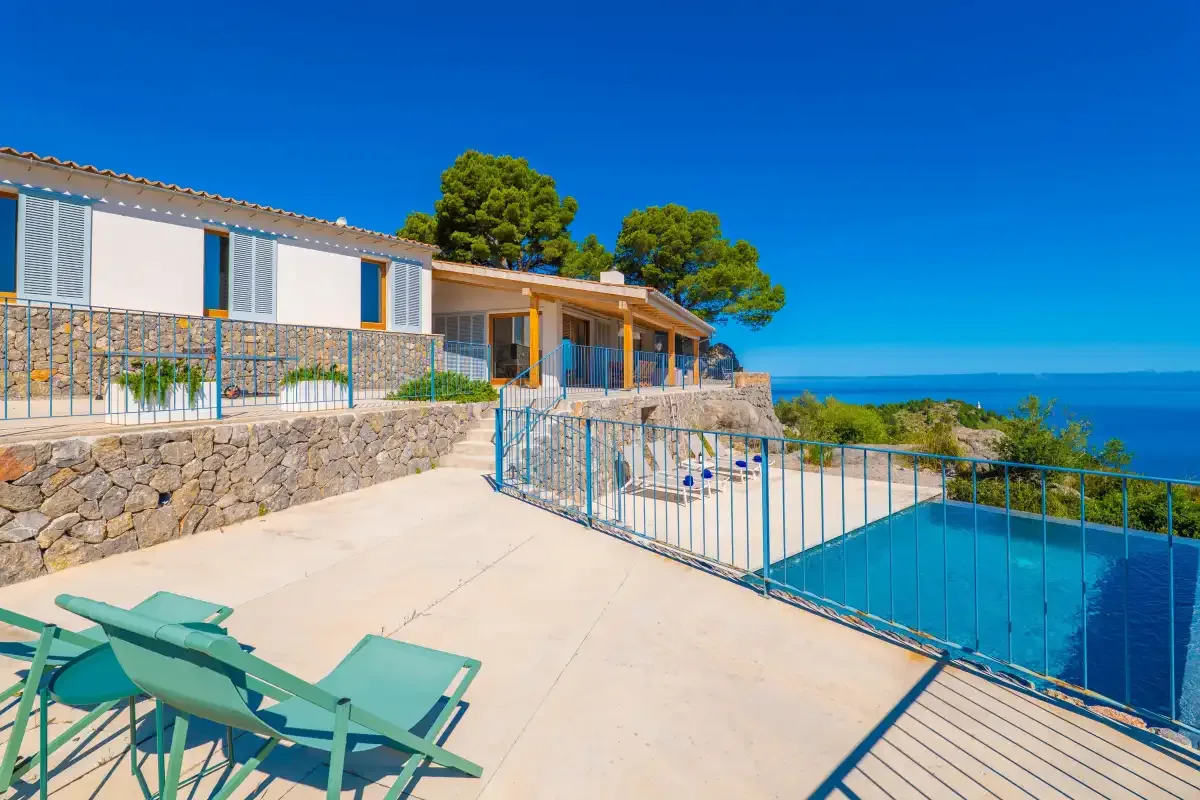 Una casa y una piscina están junto a una terraza soleada con vistas al mar.