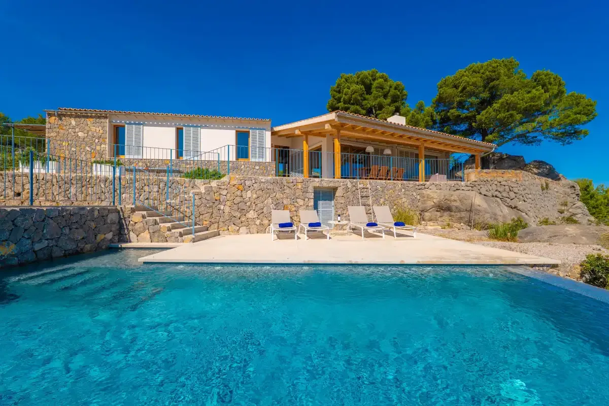 Una piscina y tumbonas están frente a una casa con muros de piedra.