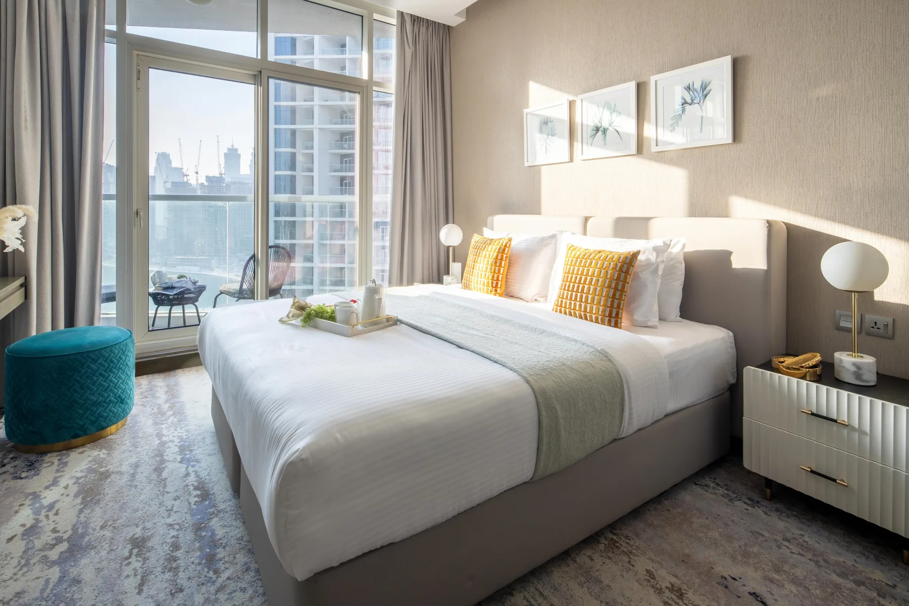 A bright bedroom features a neatly made bed beside large windows.