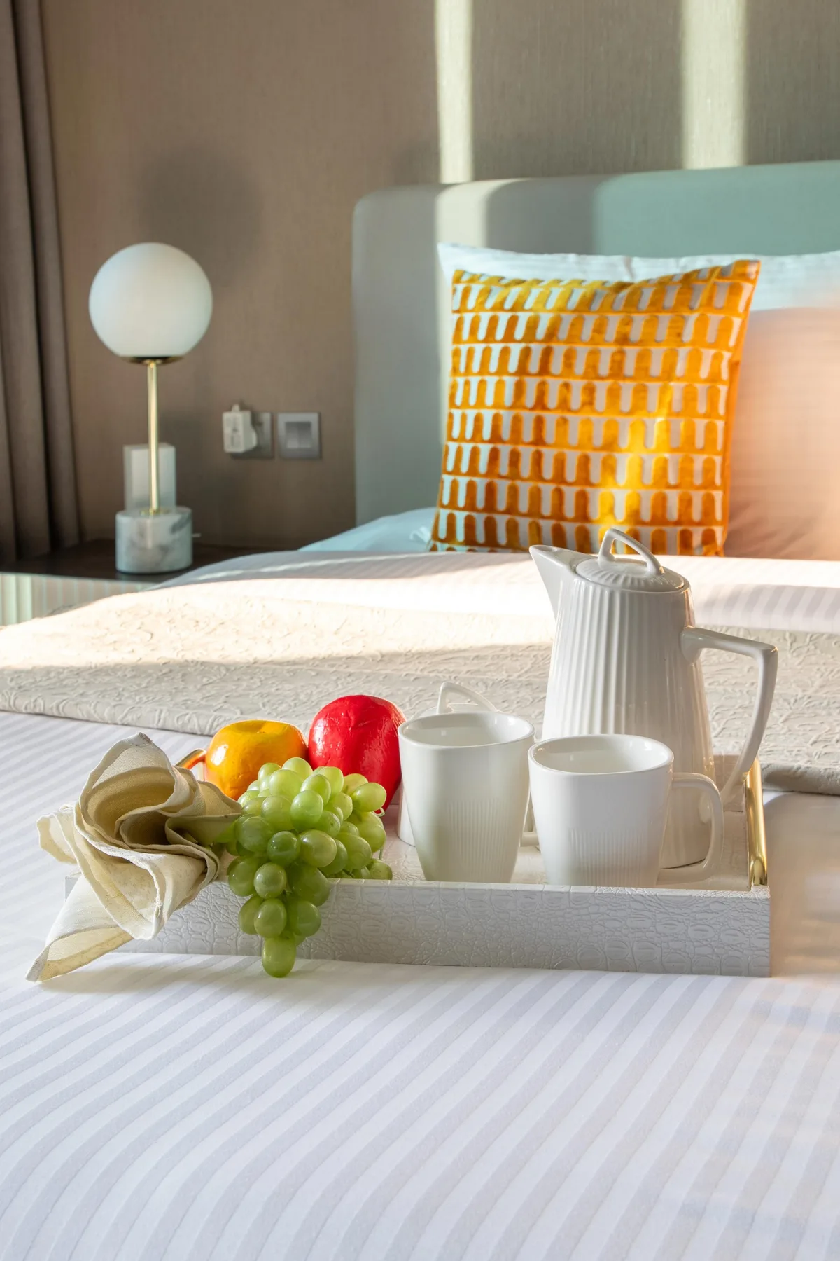 A bedroom with a breakfast tray of fruit, cups, and a teapot on the bed.