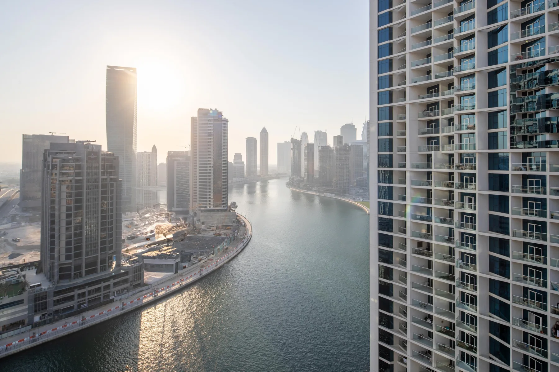 A waterfront skyline rises along a curving canal in warm morning light.