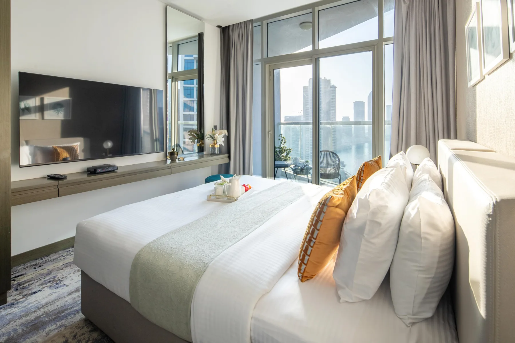 A bright bedroom with a neatly made bed beside floor-to-ceiling windows.