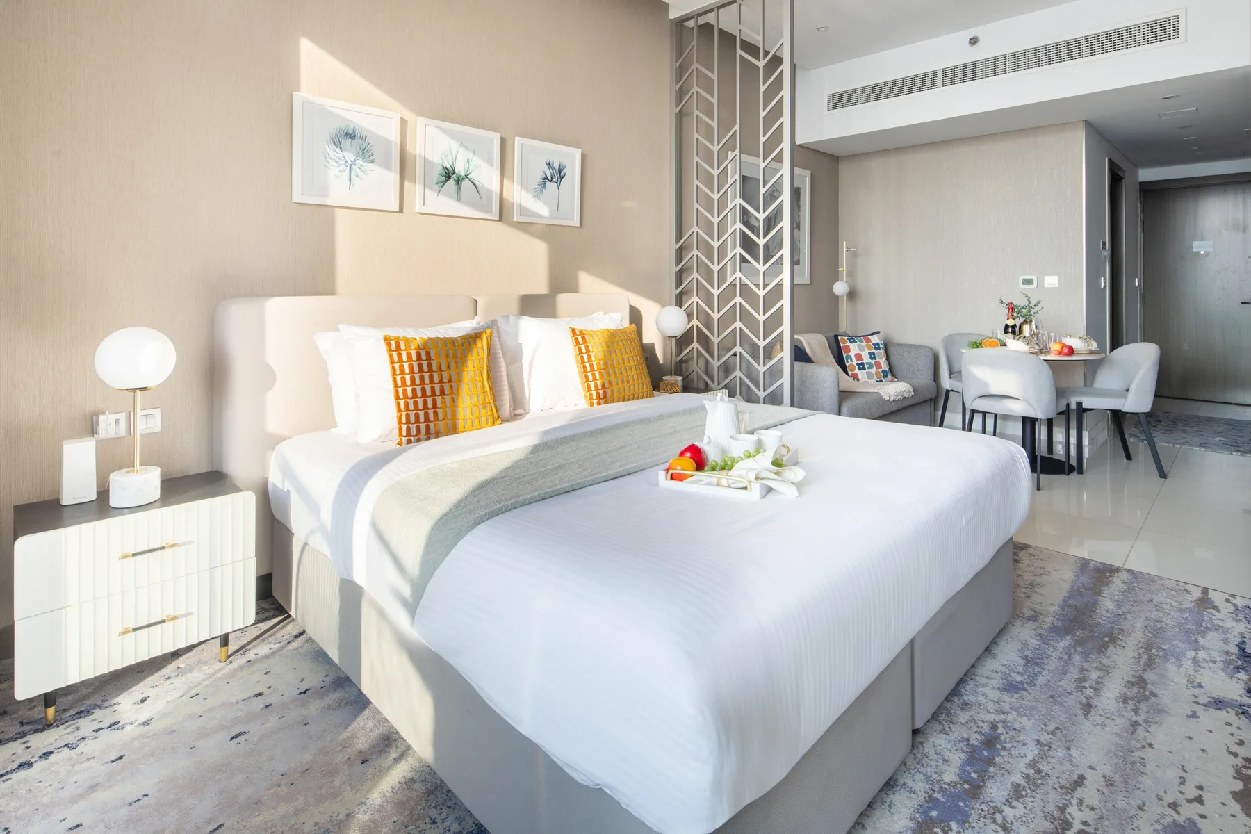 A bright bedroom with a large bed and a small dining area in the background.