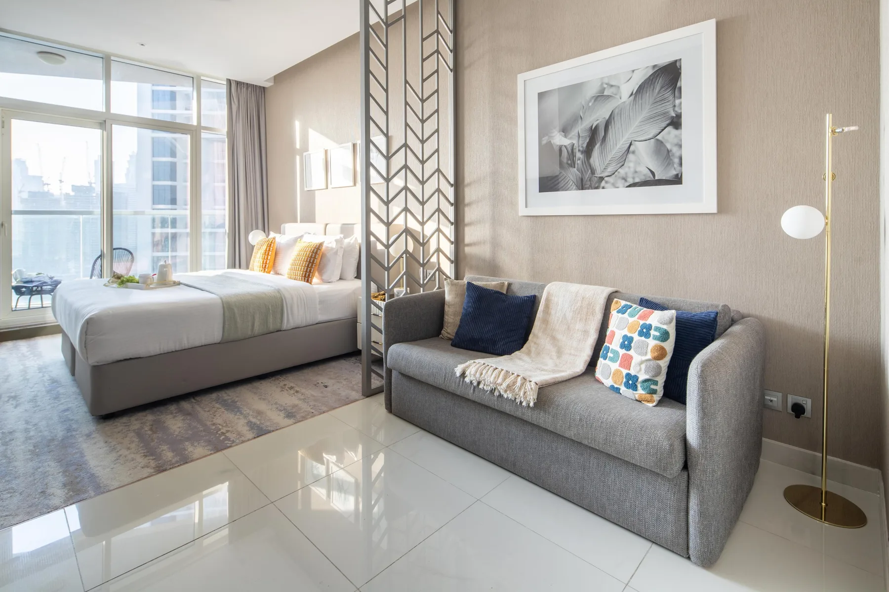 A studio bedroom and seating area with large windows and a gray sofa.