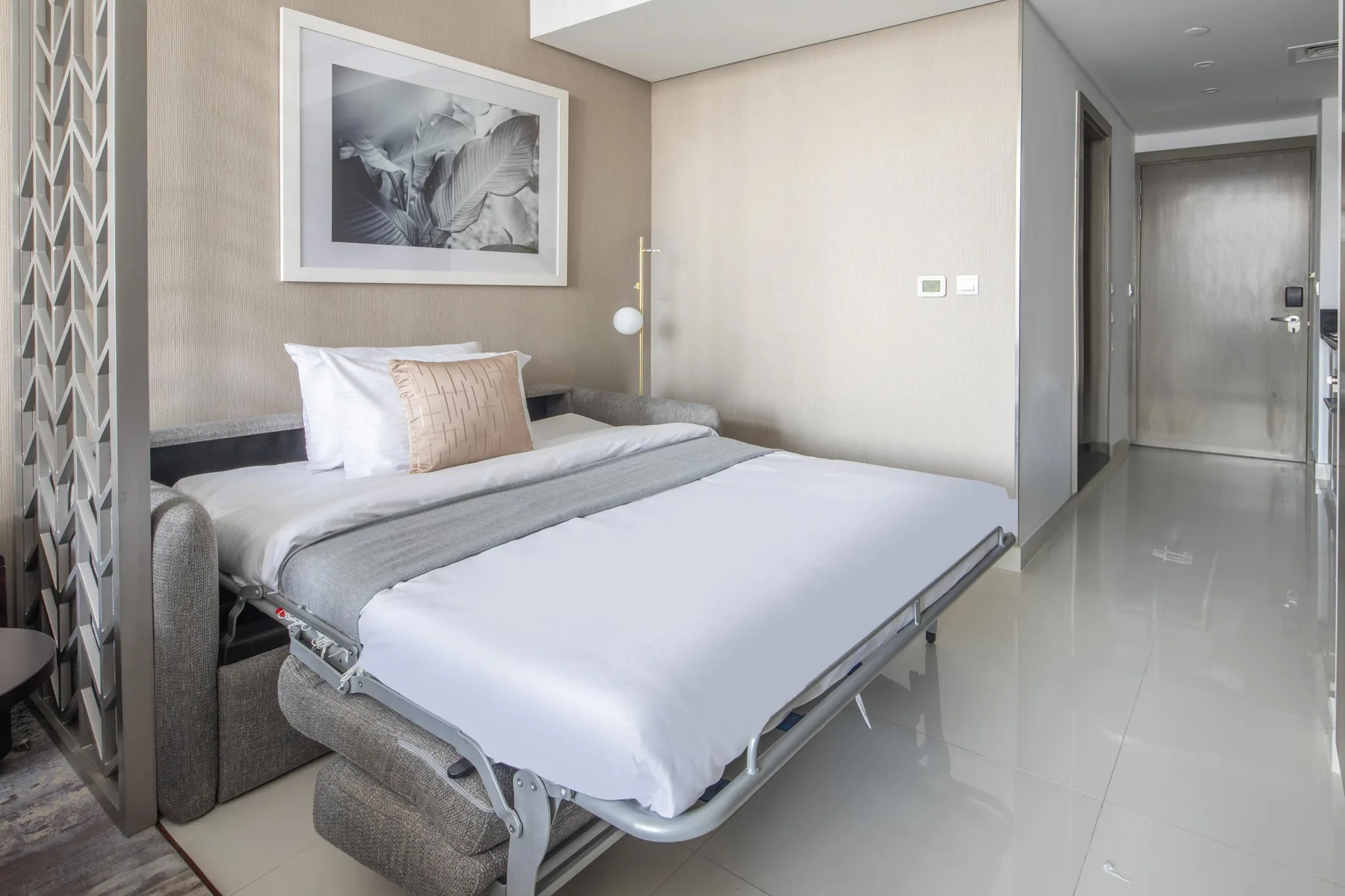 A bedroom with a bed, neutral walls, and framed artwork above the headboard.