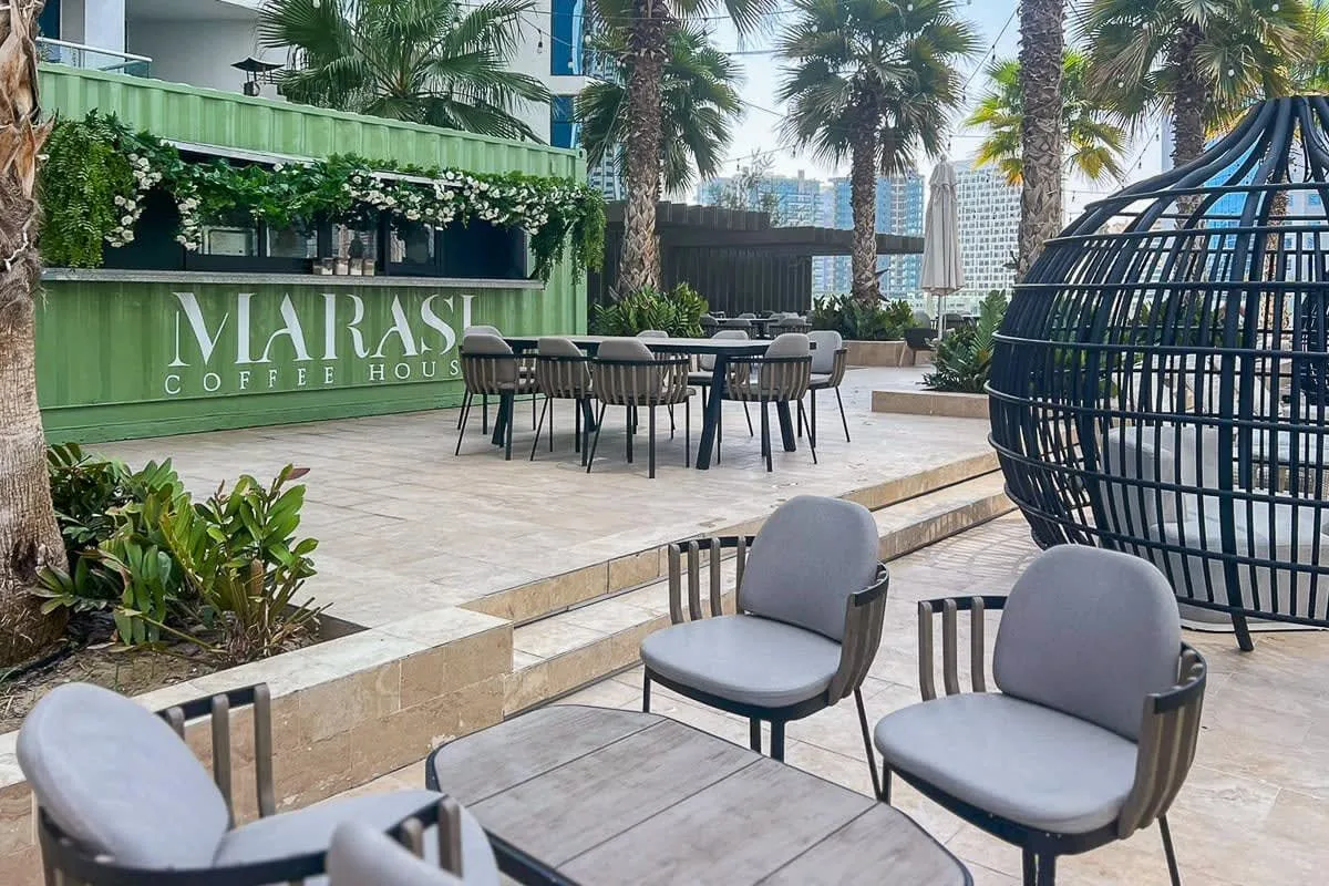 An outdoor café patio has tables and seating beneath palm trees.