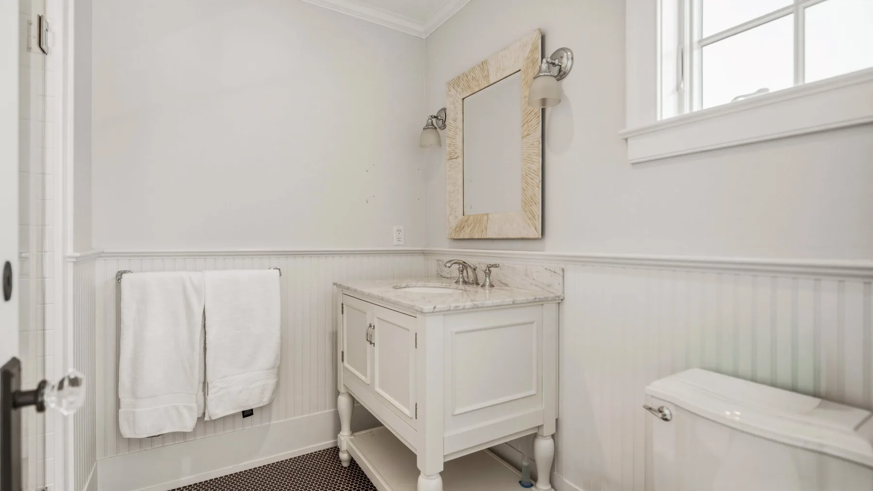 A bright bathroom features a vanity, wall mirror, and toilet.