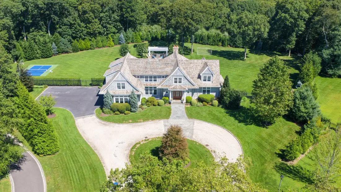 A large house sits beside a curved driveway, with lawns and trees surrounding it.