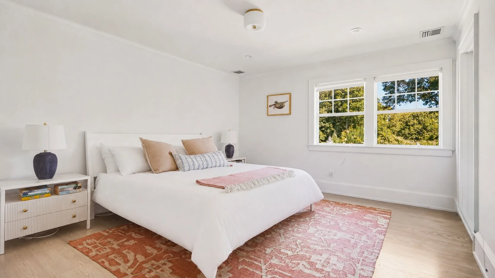 A bright bedroom with a white bed and large windows overlooking trees.