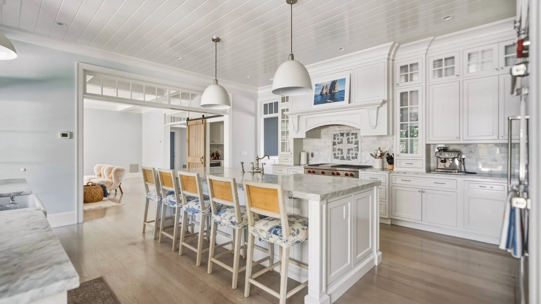 A bright white kitchen with a long island and stools beneath pendant lights.