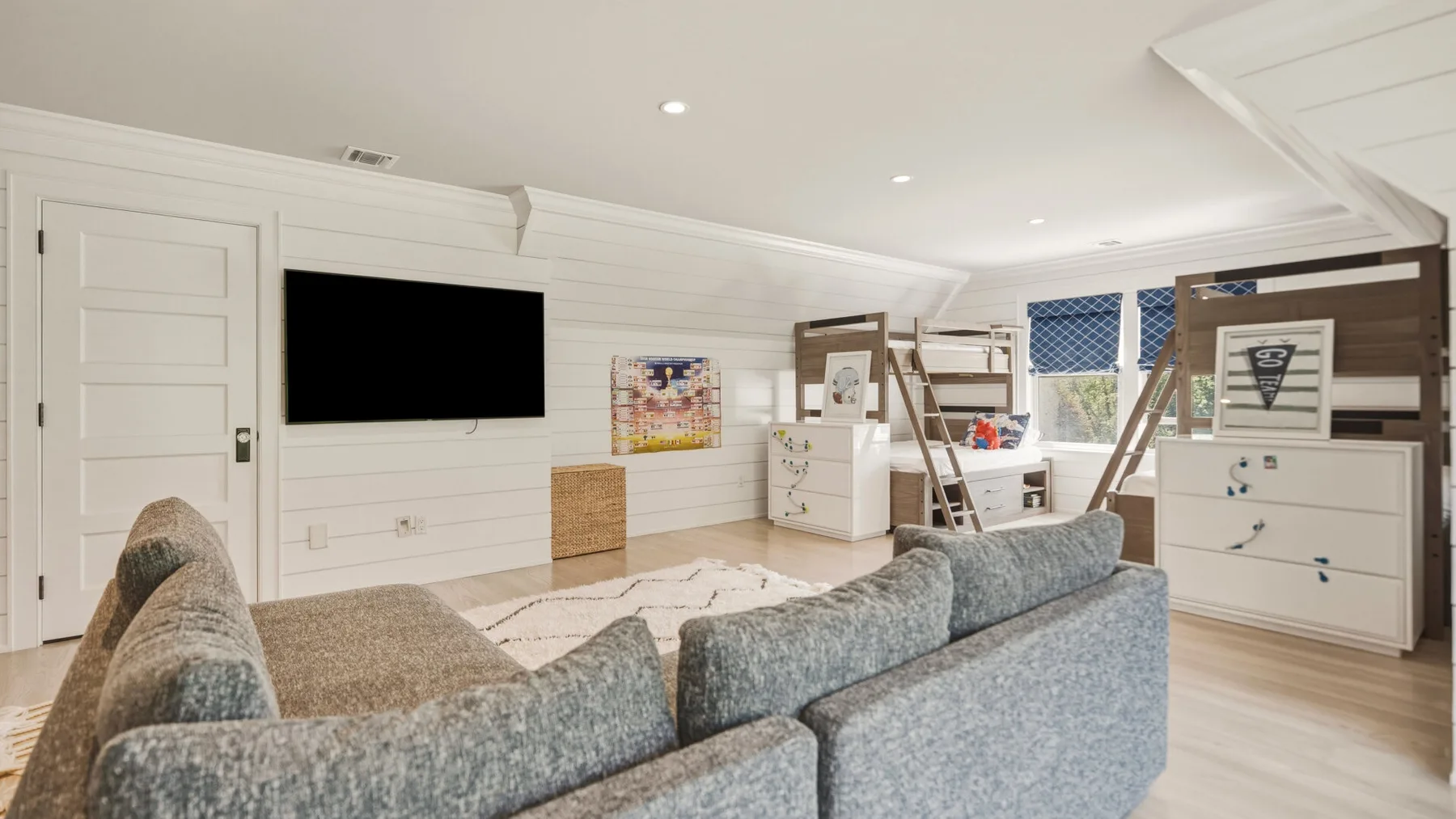 A bright bedroom with gray seating, a wall-mounted television, and bunk beds.