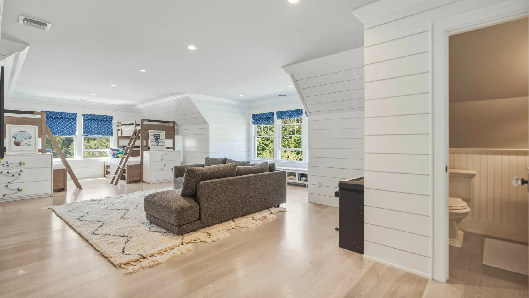 A bright attic living area with seating, large windows, and a bathroom doorway.