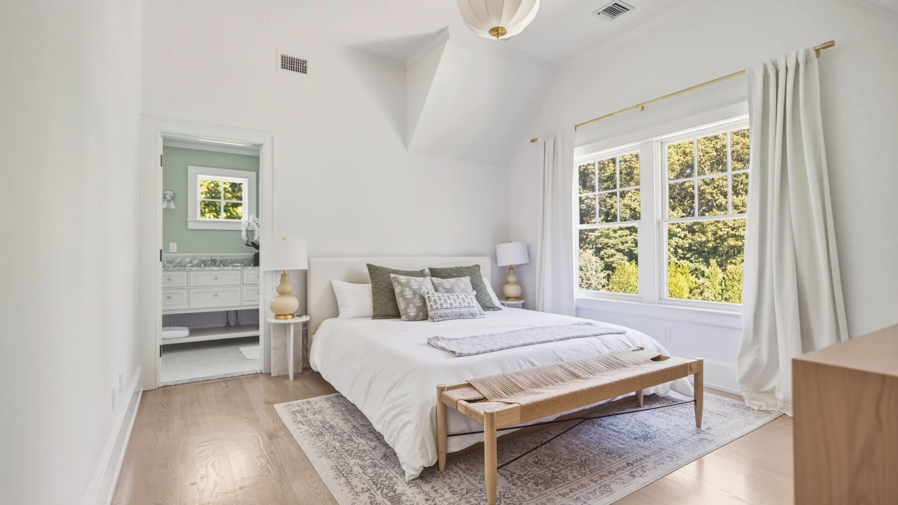 A bright bedroom with a neatly made bed beside a large window.