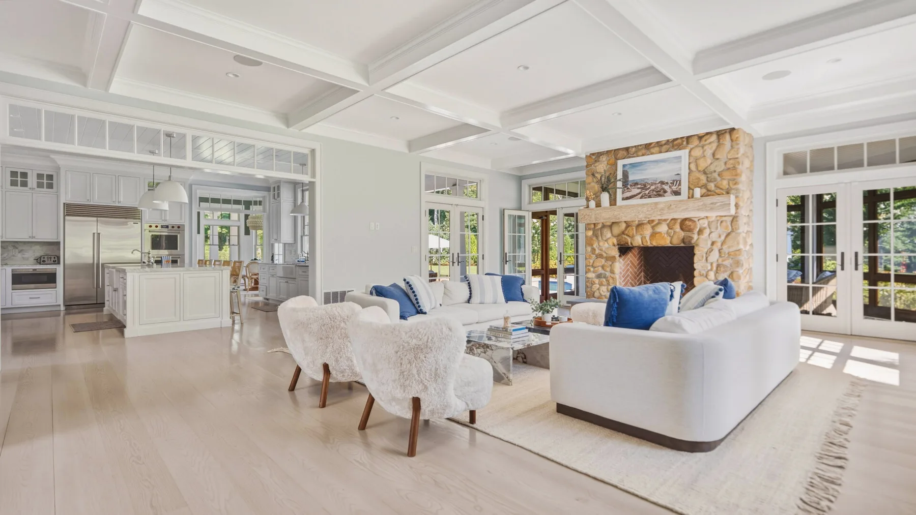 A bright open-plan living room and kitchen with seating arranged around a stone fireplace.