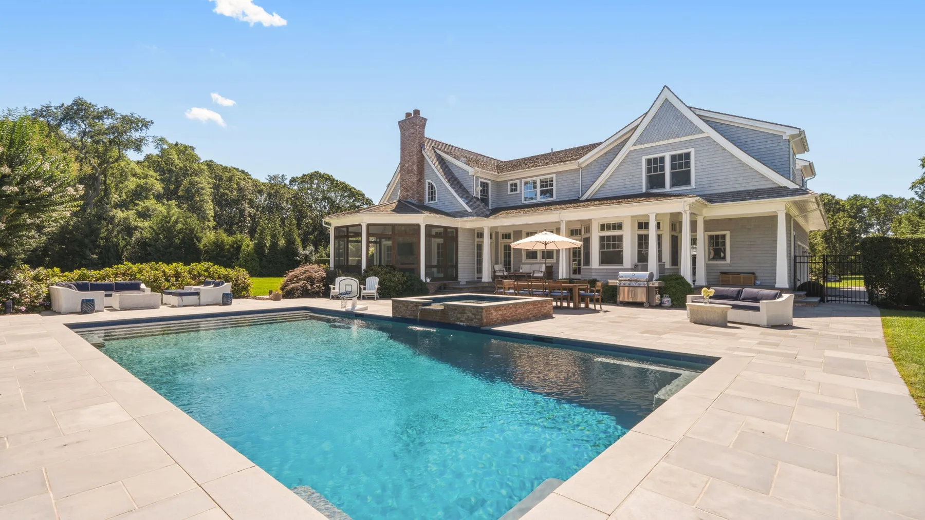 A large house stands beside a swimming pool and paved patio.