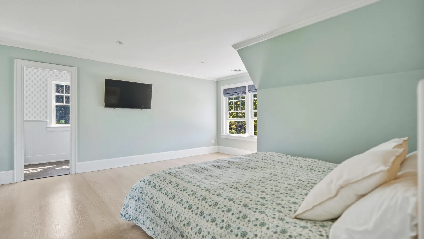 A bedroom with a bed, pale green walls, and a wall-mounted television.