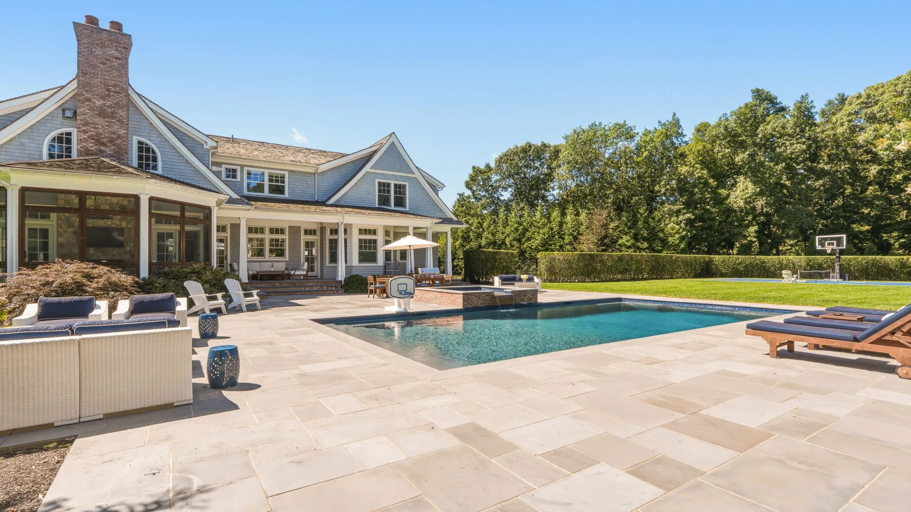 A paved patio surrounds a swimming pool beside a large house.