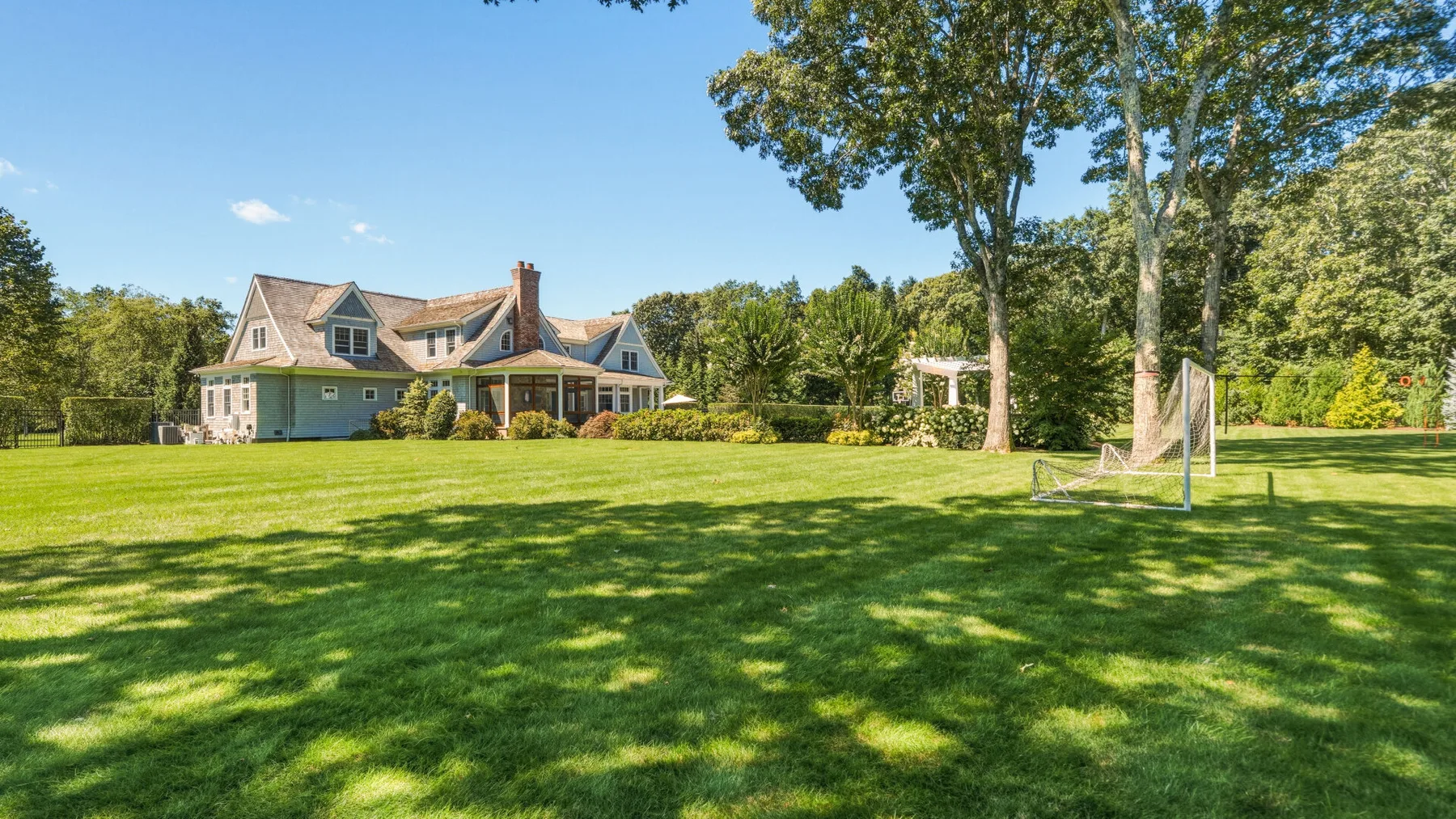 A large house stands beyond a broad green lawn and leafy trees.