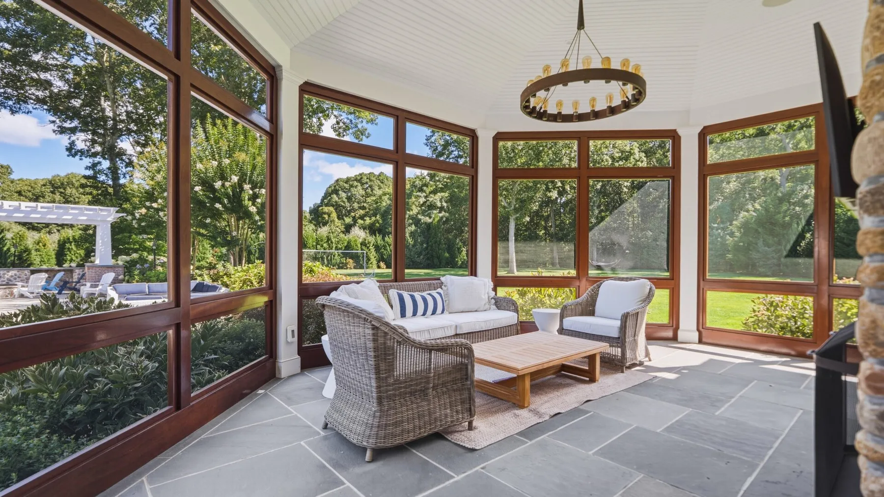 A sunroom with seating and large windows overlooking a green yard.