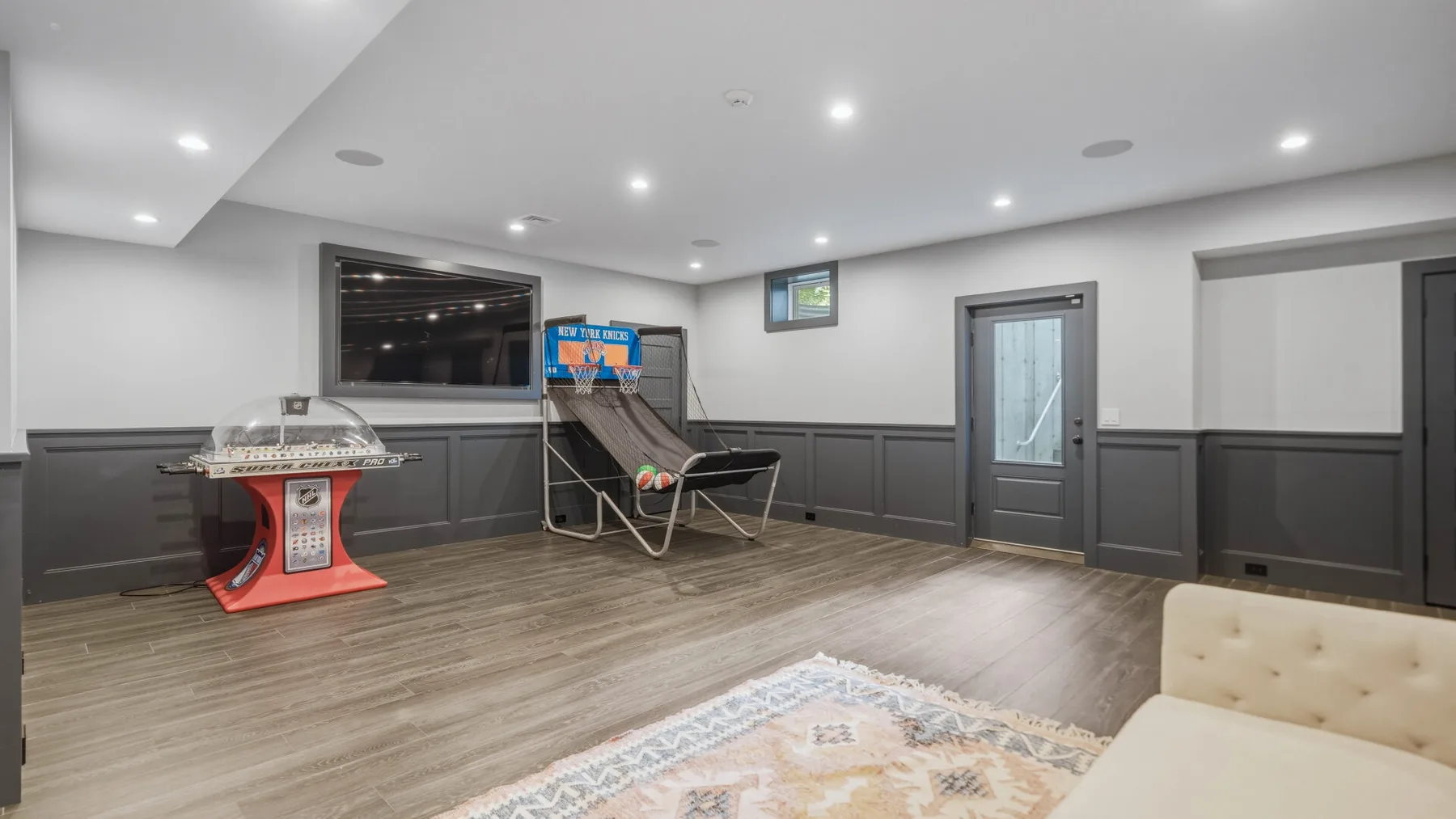 A finished basement recreation room with a pinball machine and seating.